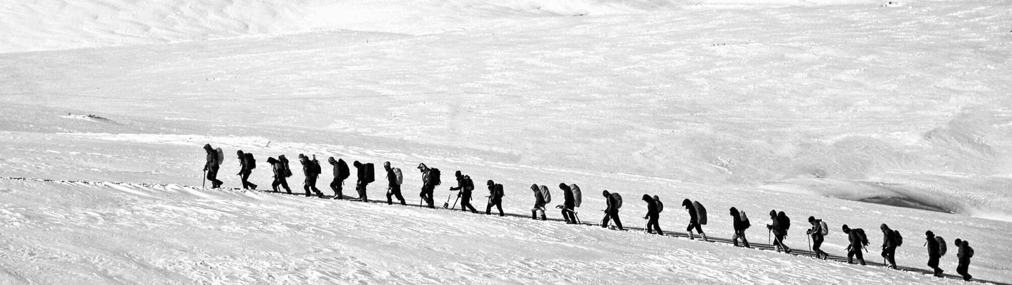 Silhouetted group hiking across a vast snowy landscape showcasing adventure and endurance.